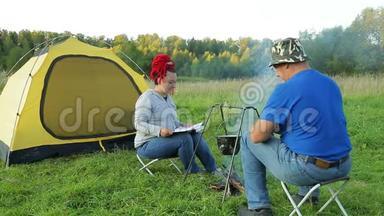 一个男人和一个女人在日落<strong>时靠近</strong>一个<strong>靠近</strong>火的帐篷，在锅里做晚餐